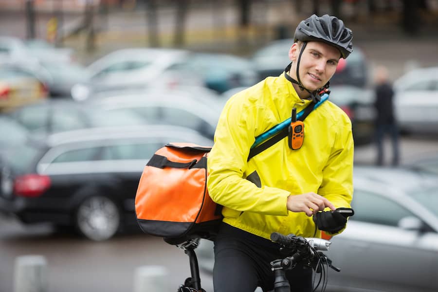Portrait of young male cyclist with courier delivery bag using mobile phone on street