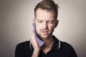: a man in pain holding a towel to his jaw